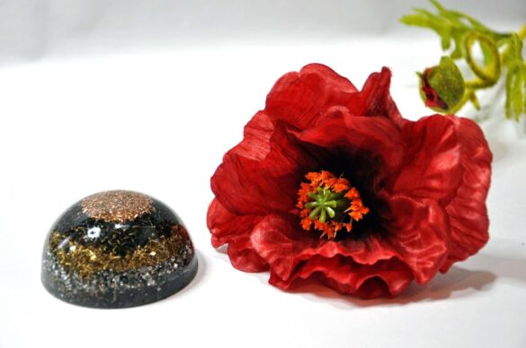 Orgonite en forme de dôme, avec un mélange de cuivre et de pierres, posée à côté d'une fleur de coquelicot rouge