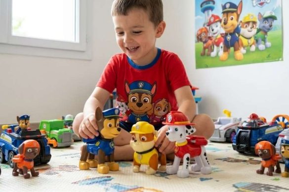Un jeune garçon assis par terre s'amuse joyeusement avec plusieurs grandes figurines de la Pat Patrouille.