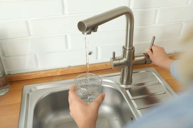 Une personne remplit un verre d'eau claire sous un mitigeur moderne installé au-dessus d'un évier en inox.